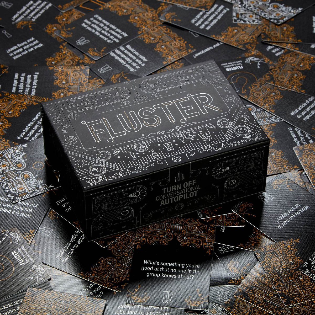 The Fluster box on top of a bunch of spread out cards with the spot UV and linen embossing reflecting the light.