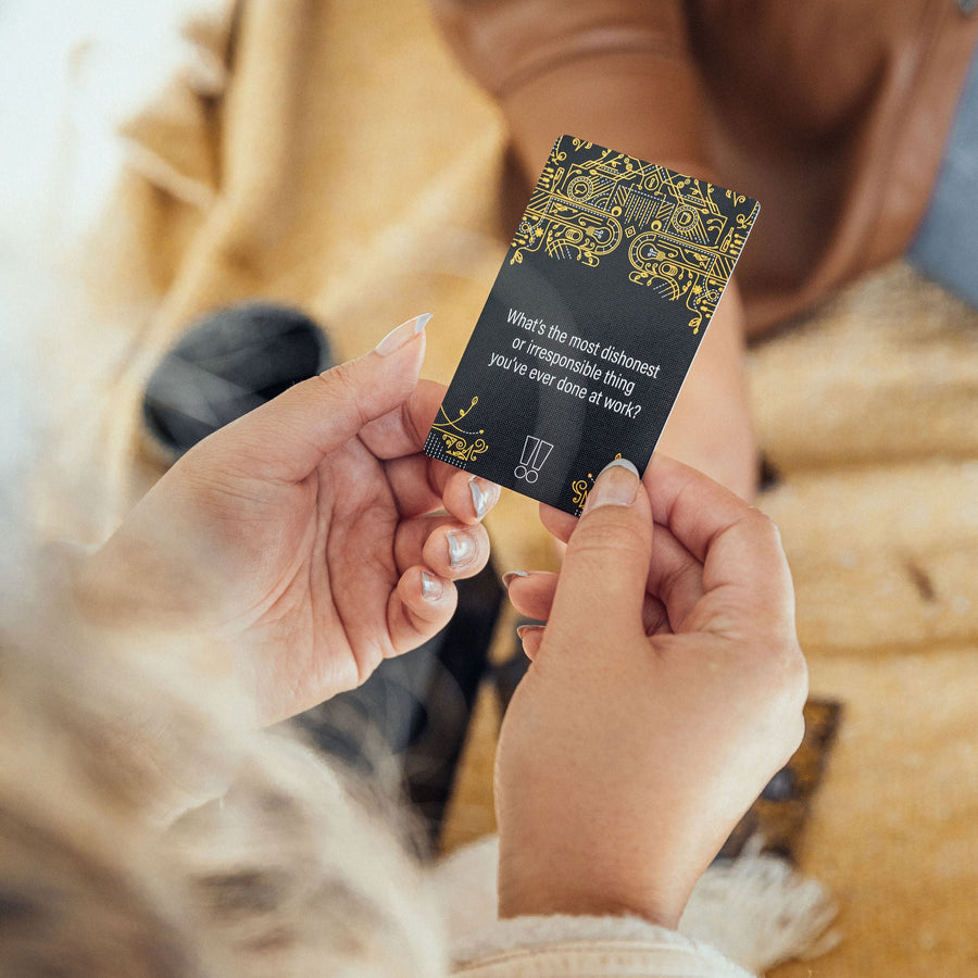 A woman holds up a question card that says "What's the most dishonest or irresponsible thing you've ever done at work?"