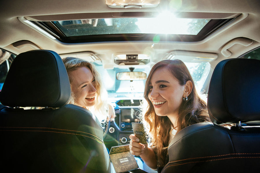 Two women in the front seat of a car holding FLUSTER cards