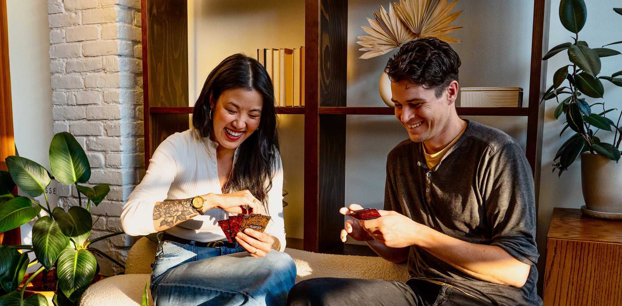 Two people sitting on a couch in a cozy room with plants and drinks.