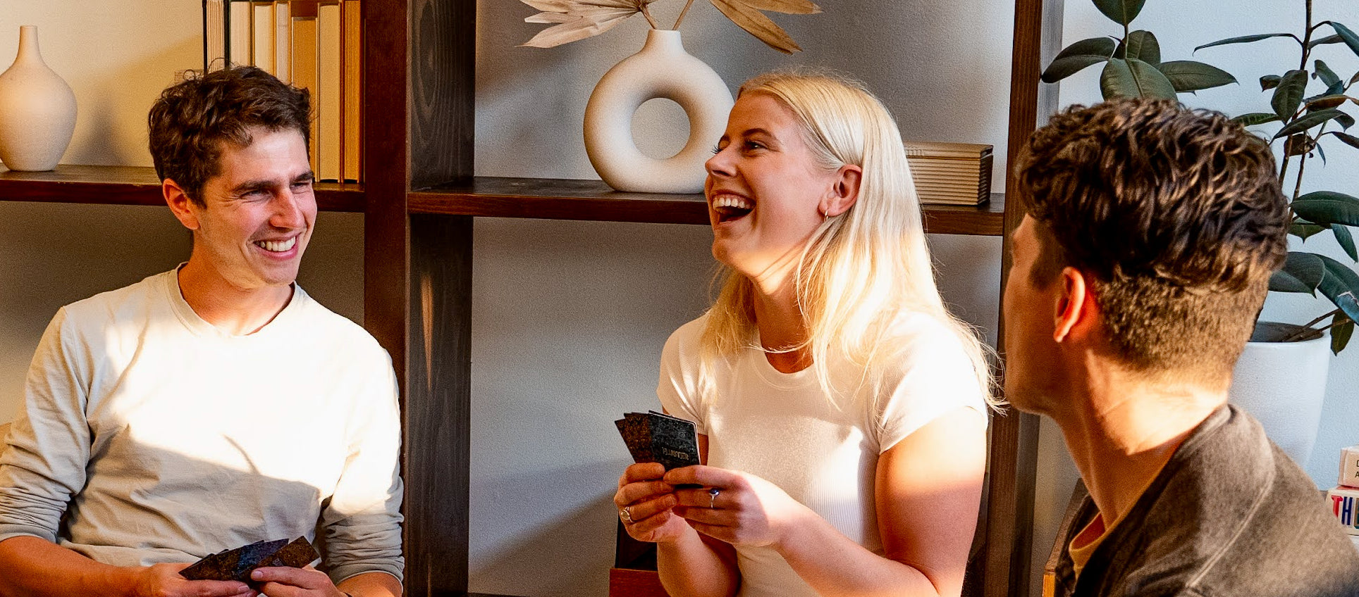 Three people sitting together, smiling and laughing in a cozy indoor setting.
