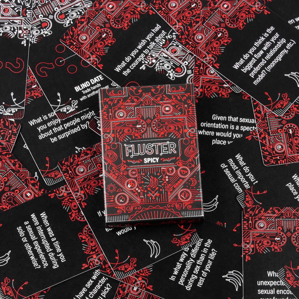 The red Fluster Laugh Pack on top of scattered cards from the deck showcasing the intricate and beautiful design.